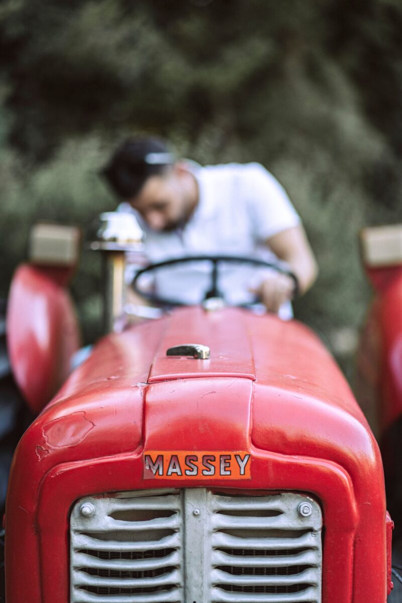 Close-up of a man sitting on a vintage red Massey tractor on a farm, showcasing agriculture machinery.
